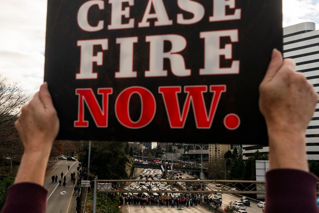 AP/Lindsey Wasson A pro-Palestinian protester holds a 'cease-fire now' sign as others block Interstate 5 northbound while calling for a cease-fire in the Israel-Hamas war Saturday, January 6, 2024 at downtown Seattle.